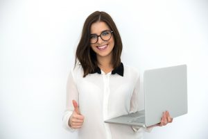 Smiling businesswoman standing with laptop and showing thumb up