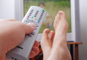 Remote control used by adult man in his hand and the legs are on the table